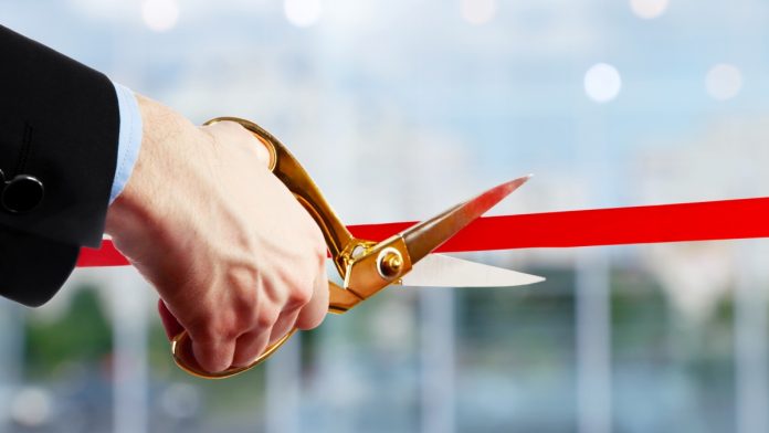 A businessman cuts a red ribbon, opening a new product