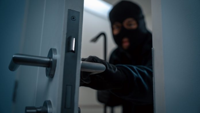 A thief in a balaclava sneaks behind a door