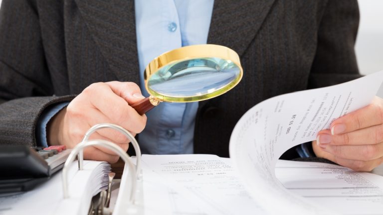 Man in suit takes a closer look at papers with a magnifying glass