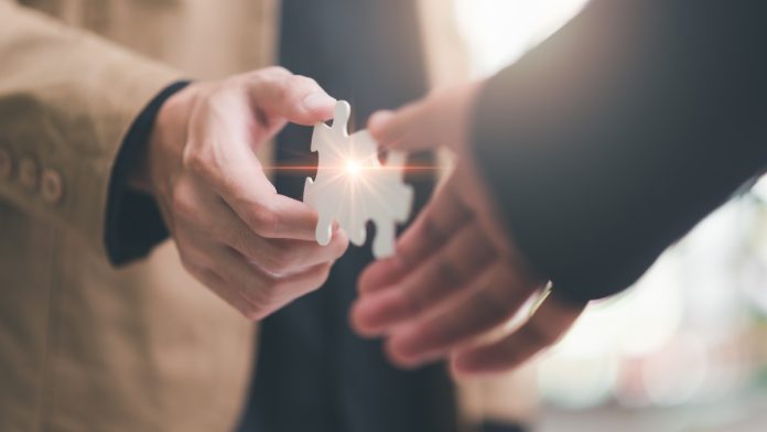 Two hands bring together puzzle pieces, indicating a partnership between the two