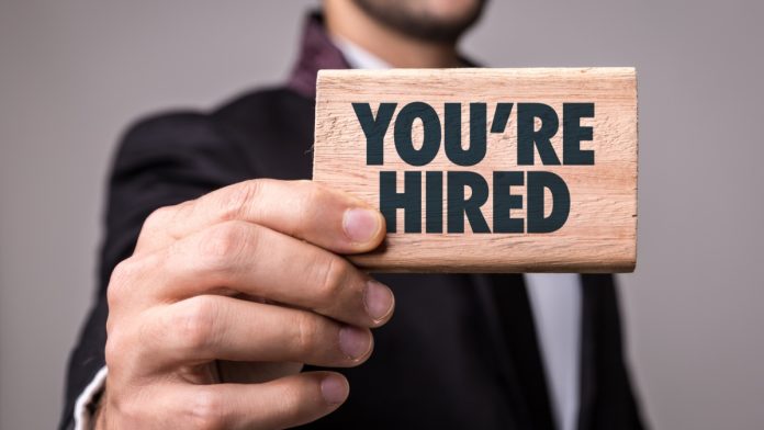 A man holds a sign that proclaims 'you're hired'