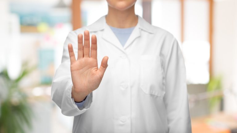 Woman in a lab coat holds her hand up, telling someone to halt