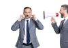 Andrew Rhodes: UK Government can’t ignore the looming crypto future Businessman shouts through megaphone at another with his fingers in his ears
