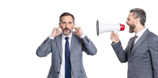 Andrew Rhodes: UK Government can’t ignore the looming crypto future Businessman shouts through megaphone at another with his fingers in his ears
