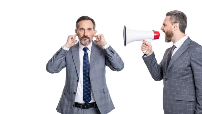 andrew-rhodes-uk-gov-looming-crypto-future Businessman shouts through megaphone at another with his fingers in his ears