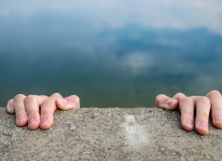 UK charities on a “cliff-edge” amidst funding shake-up Hands holding on to a cliff edge