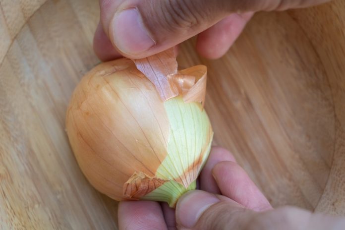Close up a hand peeling an onion