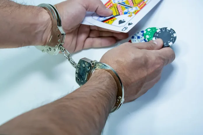Man in handcuffs holds out cards and poker chips